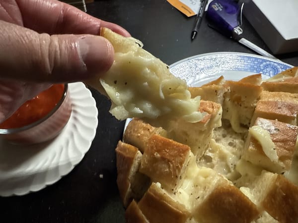A person pulls a piece of cheesy garlic break way from the loaf. The cheese is melty and there appears to be butter brushed on the surface of the loaf.