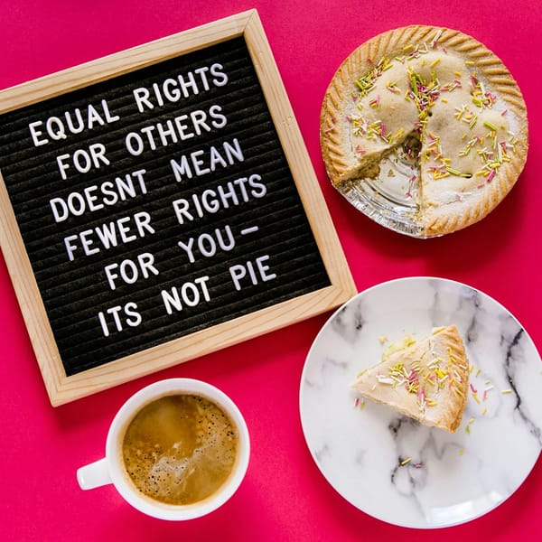 A sign says, "Equal rights for others doesn't mean fewer rights for you—it's not pie," next to a pie with a slice missing and a cup of coffee on a pink background.